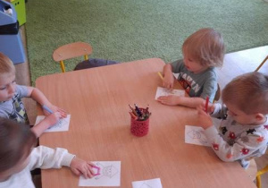 Dzieci siedzą przy stolikach w przedszkolu kolorując Krasnala Hałabałę.